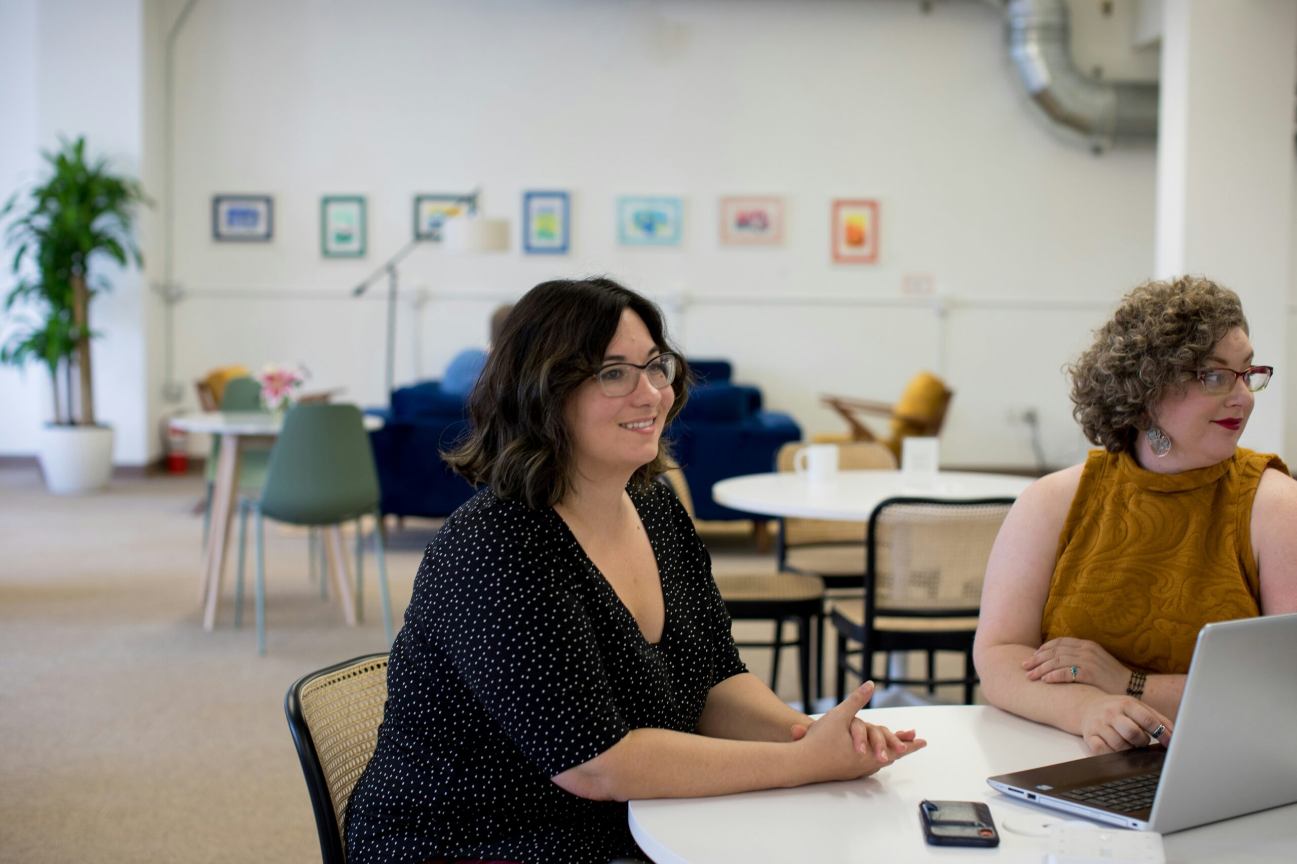 Two women at a table in an office doing new hire onboarding tasks on a laptop.